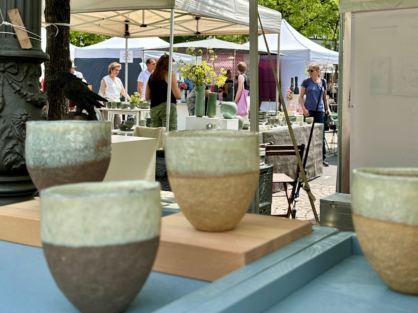 im Vordergrund 4 Becher in Naturtönen, im HIntergrund Marktstände 