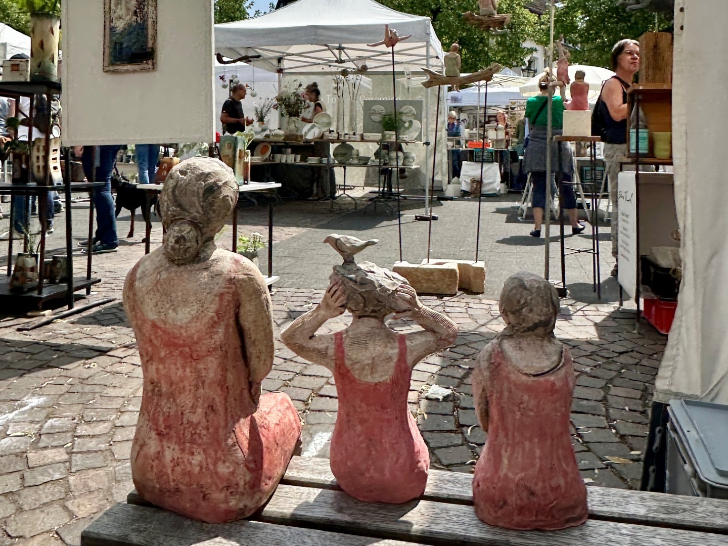 drei Figuren aus Ton sitzen auf einer Bank 