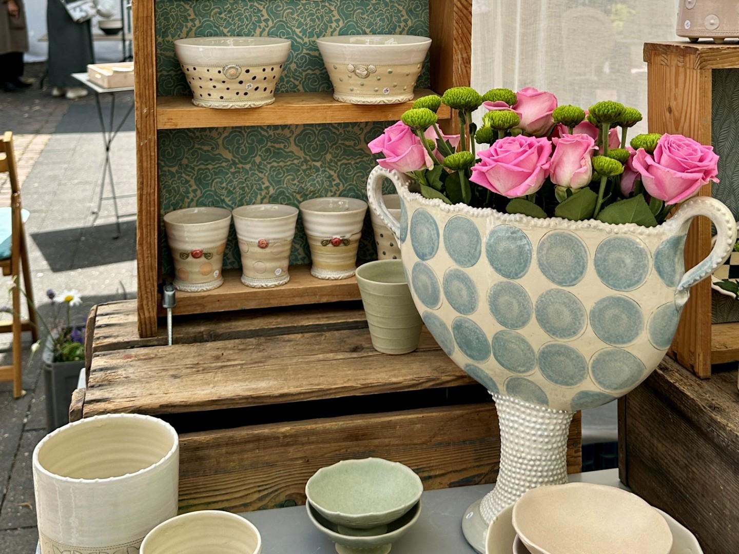 Becher in einem Holzregal, pinke Rosen in einer Vase