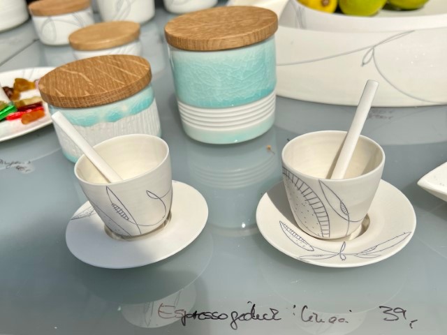 zwei Espresso Tasse in weiß mit schwarzem Muster, im Hintergrund zwei türkisfarbene Dosen