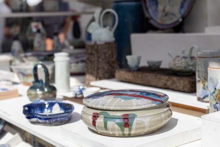 eine Keramikdose in grau und rot auf einem Tisch, im Hintergrund weitere Keramiken